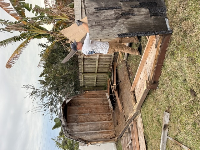 A Salty Dawgs crew member dismantling an old wooden shed.